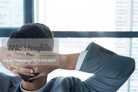 Businessman looking through window with hands behind head, rear view