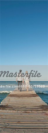 Couple walking on pier holding hands, rear view