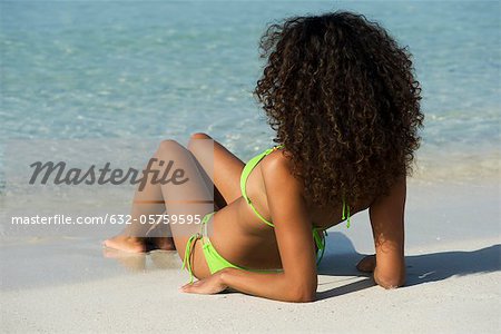 Woman relaxing on beach, looking at ocean, rear view