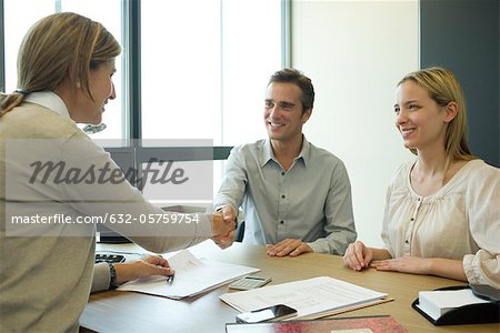 Couple shaking hands with businesswoman in office