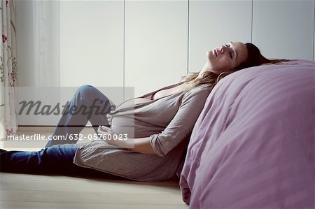 Pregnant woman leaning against bed resting