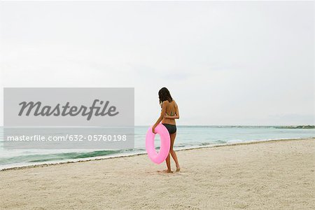 Woman standing on beach, holding inflatable ring, rear view
