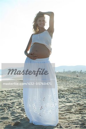 Pregnant woman standing on beach with hand on belly