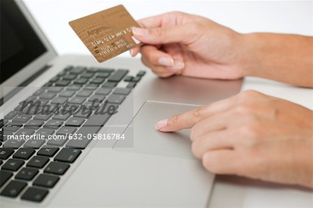 Woman holding credit card while using laptop computer, cropped