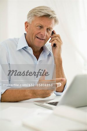 Man talking on cell phone while using laptop computer