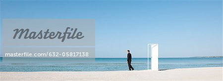 Businessman standing on beach next to half-open door, looking at ocean