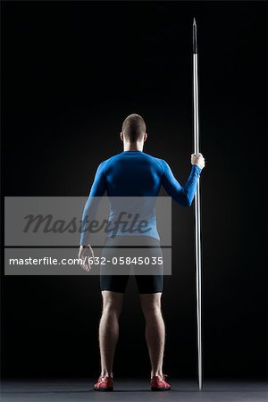 Male athlete standing with javelin, rear view