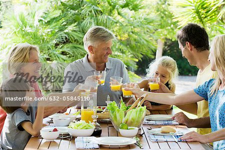 Multi-generation family toasting with orange juice outdoors, portrait