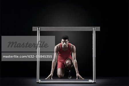 Male athlete at starting position in front of hurdle