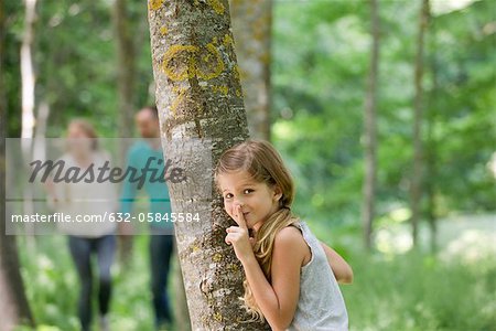 Girl hiding behind tree with finger on lips Girl hiding behind tree with finger on lips
