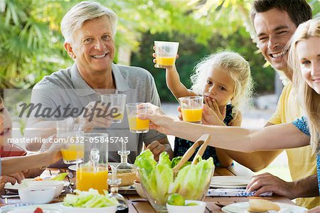 Multi-generation family toasting with orange juice outdoors, portrait