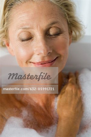 Mature woman relaxing in bubble bath with eyes closed, portrait