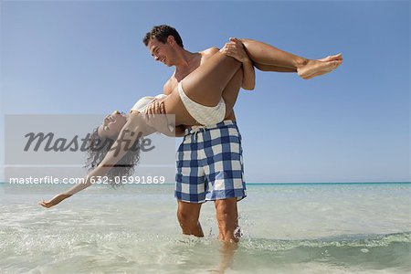 Couple together at the beach, man carrying woman in water