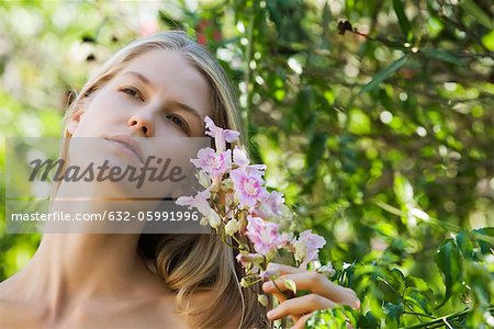 Young woman holding branch of flowers, looking up, portrait
