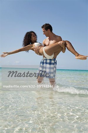 Couple together at the beach, man carrying woman