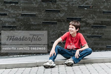 Boy sitting on sidewalk listening to music with earphones