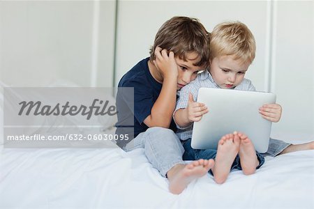 Young brothers sitting on bed looking at digital tablet