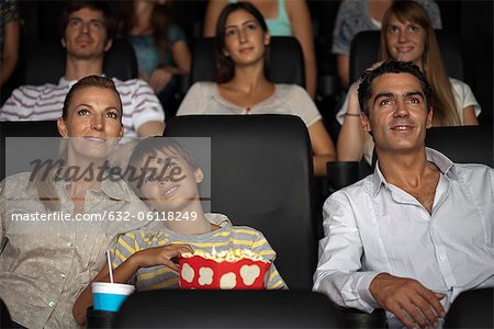 Family enjoying movie in theater, boy resting head on his mother's shoulder