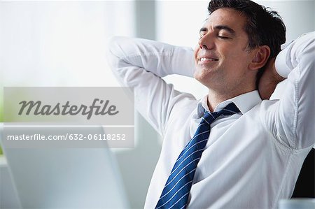 Businessman relaxing at desk hands behind head