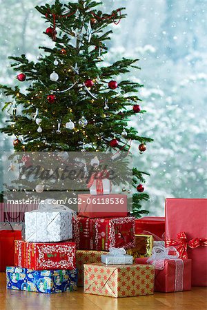 Festively wrapped gifts stacked in front of Christmas tree