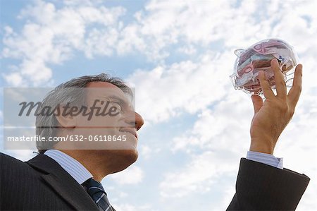 Mature man holding up transparent piggy bank filled with euros