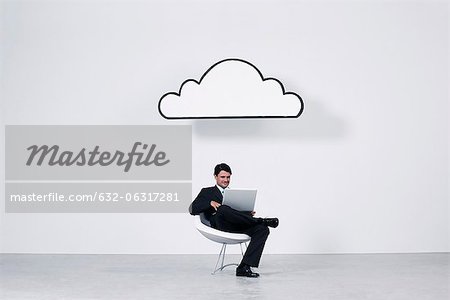 Businessman using laptop computer beneath cloud representing cloud computing Businessman using laptop computer beneath cloud representing cloud computing