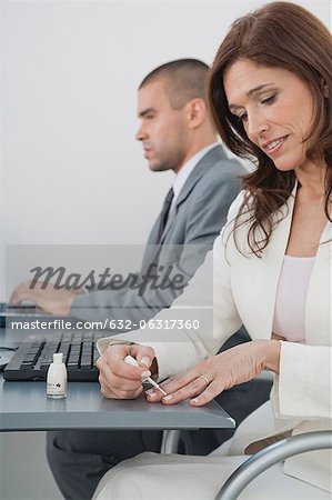 Mature businesswoman applying nail polish in office