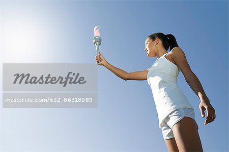 Female athlete holding up torch, low angle view