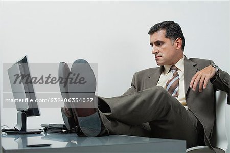 Businessman sitting in office with feet up on desk - Stock Photo