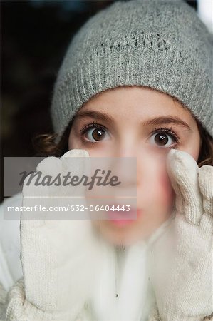 Girl breathing on window, dressed in winter clothes