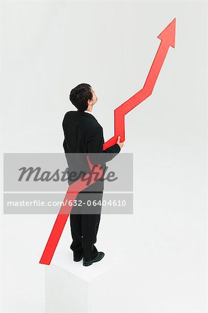 Businessman standing at top of steps holding arrow pointed upward
