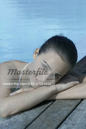 Woman in pool leaning against deck, resting head on arms