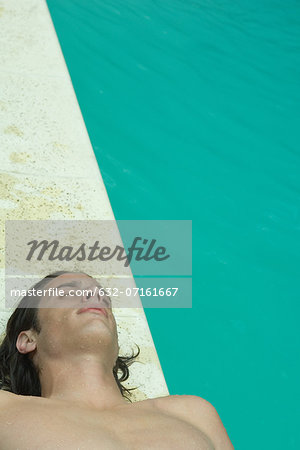 Young man lying on back beside pool