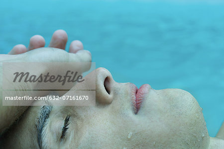 Young man touching forehead with back of hand, eyes closed, water in background