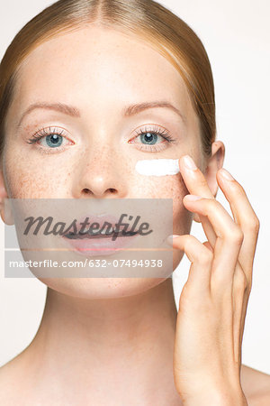 Young woman applying moisturizer under eye