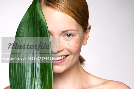 Young woman holding up leaf concealing part of face