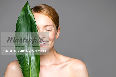 Young woman holding up leaf concealing part of face Young woman holding up leaf concealing part of face