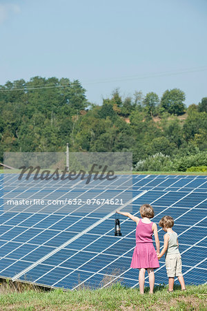 Children standing together in front of solar panels, girl holding old-fashioned latern