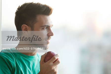 Man holding apple, gazing out window