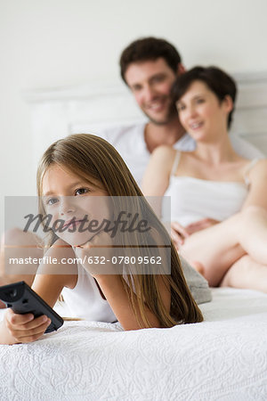 Little girl watching tv in bedroom with parents
