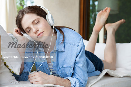 Young woma lying on stomach, listening to headphones with eyes closed Young woma lying on stomach, listening to headphones with eyes closed