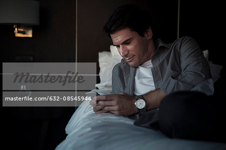 Man relaxing on bed with multimedia smartphone