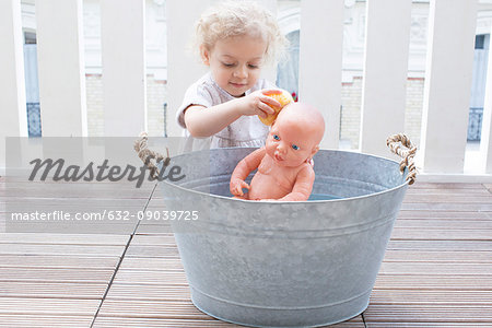 Little girl bathing baby doll in bucket outdoors