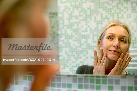 Mature woman scrutinizing her face in bathroom mirror