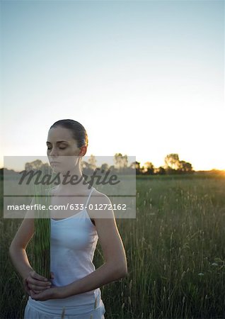 Woman standing, holding bundle of grass, eyes closed