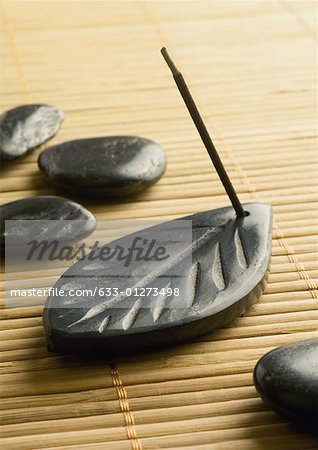 Stick of incense burning in incense holder and smooth black stones