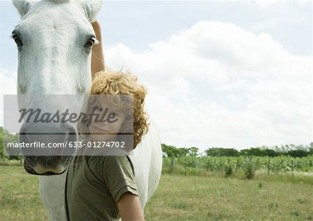 Boy standing with arm around horse