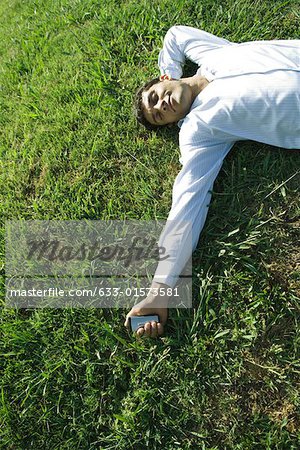 Businessman lying on grass, holding cell phone, eyes closed, smiling