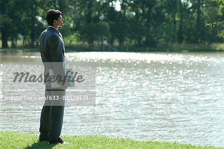 Businessman standing by edge of water, holding laZSop under arm