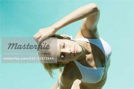 Young woman standing in bikini with hand behind head, eyes closed, high angle view